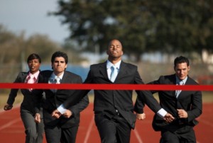 Men in suites running on a track crossing a red ribbon finish line