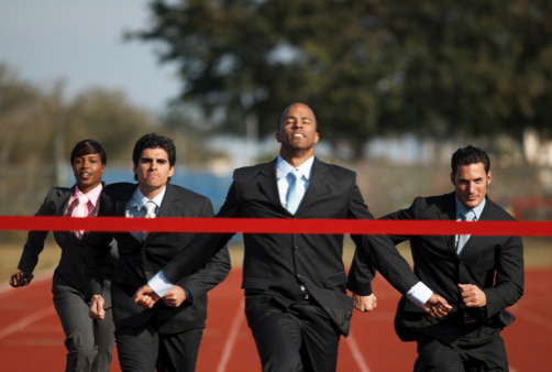 Men in suites running on a track crossing a red ribbon finish line