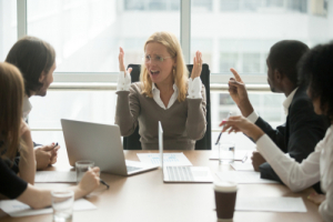 Stressed woman sitting at board table being yelled at by colleagues
