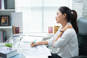 Woman working at computer holding her shoulder as if it hurts