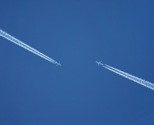 Two airplanes passing each other in the blue sky. Leaving trails of exhaust behind them.