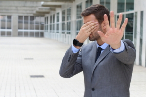 man with hand over face holding up other hand in stop motion