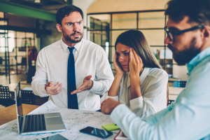 Angry white man with colleagues looking frustrated at laptop and blue prints